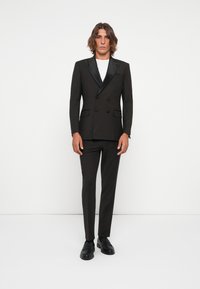 Svart dobbeltspent dress med sateng sjal-lapper, slim-fit bukser og svarte loafers. Modellen har på seg en hvit T-skjorte under.