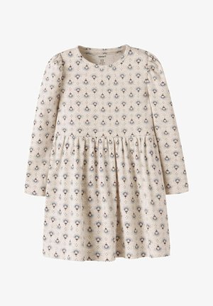 Pitkähihaista mekkoa vaaleanbeigessä kankaassa, jossa on herkkä kukkakuosi sinisen ja ruskean sävyissä, kerrottua vyötäröä ja pehmeää tekstuuria.