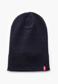 Donker marineblauwe gebreide beanie met een afgeronde bovenkant en omgeslagen rand. Heeft een klein rood label aan de zijkant. Materiaal lijkt zacht en gestructureerd.