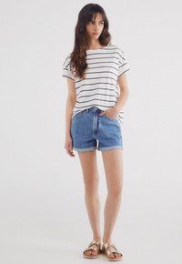Striped white and navy short-sleeve t-shirt paired with light blue denim shorts. The shorts are folded at the hem. Tan sandals complete the look.