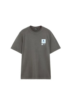 Camiseta de manga corta de color gris oscuro con cuello redondo y un pequeño parche azul claro con un gráfico de calavera y tibias cruzadas en el pecho izquierdo.