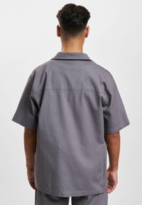 Kortærmet skjorte med krave i medium grå stof, der har en afslappet pasform og detaljeret bagsøm. Enkelt design uden synlige mønstre.