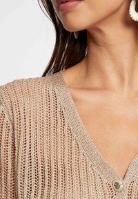 Strickjacke mit offener Webart in hellbeige, mit V-Ausschnitt und einer einzelnen Knopfleiste. Die Textur ist luftig mit einem schichtigen Design.