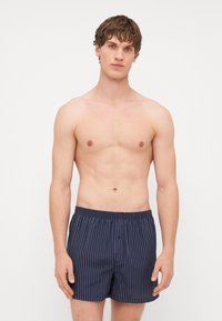 Boxer de riscas em azul-marinho com um cós elástico, apresentando um botão e um corte solto para conforto. O tecido tem uma textura suave.