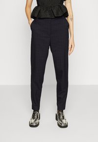 Marinblå rutiga byxor gjorda av lättviktsmaterial, med en tapered passform, sidofickor och en slät yta. Byxorna är matchade med skinande silverskor.