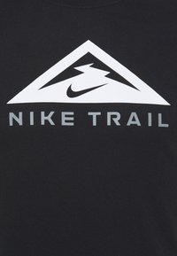Camiseta negra con un logo triangular blanco que incluye un swoosh y el texto "NIKE TRAIL" en gris claro, fabricada con suave algodón.