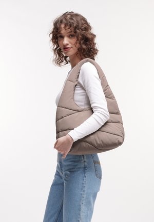 Braune Puffer-Tasche mit gestepptem Design, runder Form und seitlichem Tragegriff. Das Material wirkt weich und strapazierfähig, mit einem minimalistischen Stil.