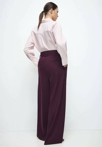 Lichtroze blouse met lange mouwen, gecombineerd met hoogtaille wijde maroon broek met een gladde textuur en subtiele details.