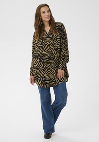 Langärmelige Bluse mit Animal-Print in Schwarz- und Brauntönen. Kombiniert mit blauen Jeans und schwarzen Schuhen, für einen lässigen Look.