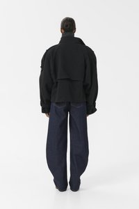 Zwarte oversized jas met een hoge kraag en een gelaagd ontwerp aan de achterkant, gecombineerd met loszittende donkerblauwe spijkerbroek.
