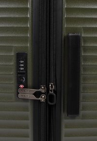 Valigia rigida verde oliva con scanalature verticali, doppie cerniere nere e un lucchetto combinato TSA sul lato per la sicurezza.