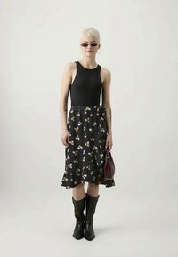 Un haut sans manches noir associé à une jupe noir à volants avec des motifs floraux jaunes et blancs. Des bottes de cowboy noires et un sac à main bordeaux.