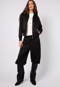 Czarna kurtka bomber z nadrukiem w panterkę, noszona na bia�łej bluzce, zestawiona z luźnymi czarnymi spodniami i błyszczącymi, sięgającymi do kolan kozaki.
