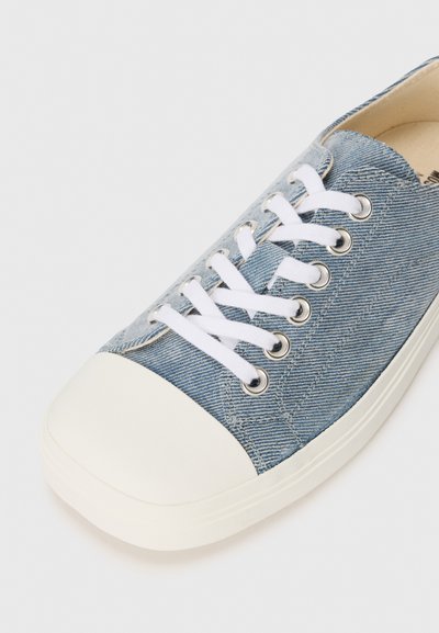 Madala tipuga spordijalanõud helesinise denimpinnaga, valge kummine varbasaam, valged paelad ja valge tald valgel taustal.