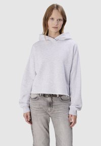 Sweat à capuche court gris clair avec capuche, poignets côtelés et texture douce, associé à un jean gris délavé et une ceinture décorative à clous.