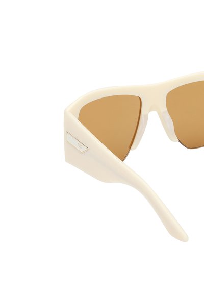 Gafas de sol de color crema con forma geométrica, lentes tintados marrones y un detalle metálico en el lateral. Montura de plástico suave y brillante.