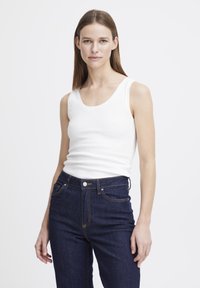 Weißes, geripptes Tanktop mit rundem Ausschnitt, kombiniert mit dunkelblauen High-Waist-Jeans mit Kontrastnähten und Fronttaschen.