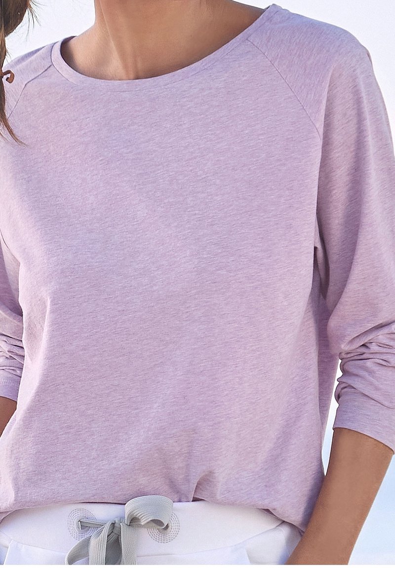 Jasnofioletowa bluzka z długim rękawem, o zaokrąglonym dekolcie i rękawach raglanowych. Miękka, teksturowana tkanina. W zestawie z białym detalem w talii.