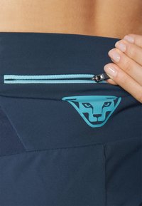 Marinblå sportshorts med en ljusblå dragkedjeficka och logotyp. Har en texturerad panel på sidan och en slät tygfinish.