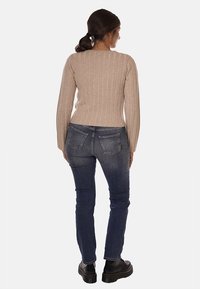 Maglione beige a coste con maniche lunghe, abbinato a jeans in denim scuro e stivali con plateau neri, visto da dietro.