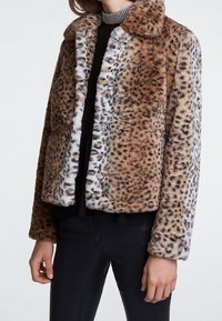 Veste en fausse fourrure imprimé animal marron et blanc, avec fermeture boutonnée, longueur courte et surface douce et texturée.