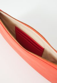 Coral leather clutch with a zipper closure; features a smooth exterior and a contrasting red cardholder inside on a beige lining.