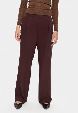 Burgundy wide-leg trousers made from soft fabric, featuring front pleats and an elastic waistband. Worn with a fitted brown top.