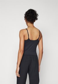 Zwarte mouwloze tanktop met dunne verstelbare bandjes, soepele textuur, aansluitend ontwerp, gecombineerd met zwarte loszittende broek.