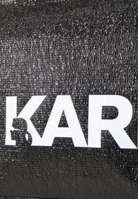 Juodas tekstūruotas maišas su ryškiu baltu logotipu, kuris skaito „KAR“, su šalia esančiu silueto dizainu.