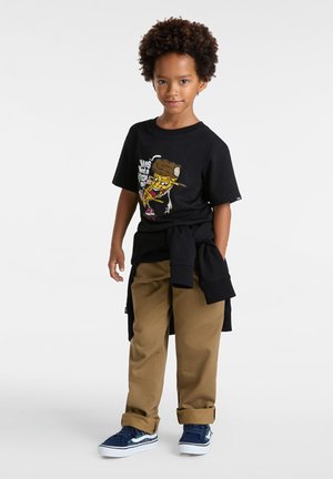 Zwart T-shirt met korte mouwen en een grafische print, beige broek en blauwe sneakers. Een zwarte trui om de taille geknoopt voegt extra lagen toe.
