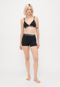 Čierny bralette s nastaviteľnými ramienkami, so vzorom loga; v kombinácii s čiernymi boxer šortkami, oboje vyrobené z hladkej, elastickej tkaniny.