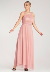 Maxi sukienka w miękkim różowym kolorze, z dopasowanym topem z zakładkami, szerokimi ramiączkami oraz zwiewną, przezroczystą spódnicą. Czarne szpilki dopełniają stylizację.