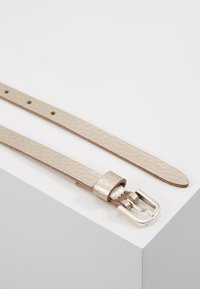 Ceinture en cuir beige avec une finition texturée, dotée d'une boucle en métal argenté et d'une seule boucle. Longueur ajustable avec plusieurs trous.