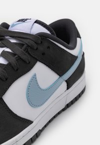 Sneaker bianco e nero con tomaia texturizzata, Swoosh in pelle azzurro chiaro, lacci grigi e suola in gomma. Presenta colletto e linguetta imbottiti.