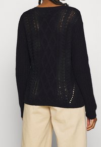 Pull marine foncé avec motif torsadé texturé, comportant des détails ajourés et une coupe décontractée. Manches longues et ourlet côtelé.