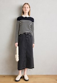 Sötétkék és fehér csíkozott, hosszú ujjas pulóver fehér gallérral, fekete farmer midi szoknyával és bézs loaferekével párosítva, egy kicsi táskával a kezében.