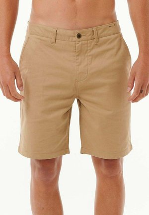 Uomo che indossa pantaloncini beige fino al ginocchio con bottone e tasche, in piedi con le mani rilassate ai lati.