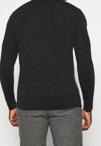 Dunkelgrauer gestrickter Pullover mit einem figurnahen Design. Lange Ärmel und ein runder Halsausschnitt. Kombiniert mit gemusterten karo Hosen.