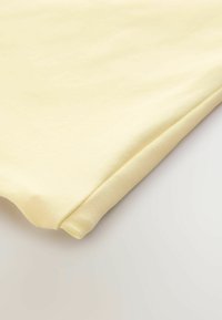 Gaiši dzeltena kokvilnas auduma salocītas, gluda tekstūra, ar mīkstu apdari un tīrām malām, ar vieglu spīdumu.