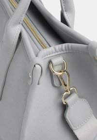 Borsa a tracolla in pelle grigia chiara con superficie testurizzata, zip dorata e tracolla removibile con clip in metallo dorato.