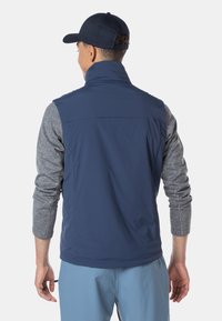 Marineblaues Westchen aus leichtem Material mit hohem Kragen. Graues Langarmshirt darunter, mit einem strukturierten Muster. Lässiger Stil.