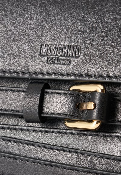 Μαύρο δερμάτινο υφή με ανάγλυφο λογότυπο Moschino Milano και μαύρο δερμάτινο λουράκι περασμένο μέσα από χρυσή αγκράφα.