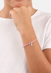 Bracciale rosa realizzato in corda, con charm in tonalità argento, tra cui una figura e un piccolo gioiello, annodato e fissato attorno a un polso.