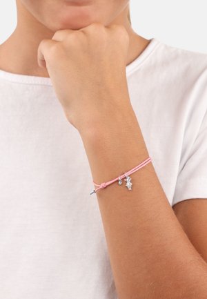 Bracciale rosa realizzato in corda, con charm in tonalità argento, tra cui una figura e un piccolo gioiello, annodato e fissato attorno a un polso.