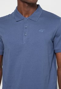 Niebieska koszulka polo wykonana z bawełny, z kołnierzykiem i zapięciem na trzy guziki. Posiada subtelne logo 4F na piersi. Krótkie rękawy.