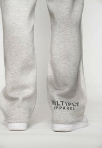 Szare dresy o miękkiej teksturze, luźnym kroju oraz czarnym napisem "MULTIPLY APPAREL" w okolicy kostki, zestawione z białym obuwiem.