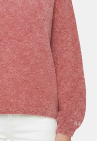 Maglione rosso lavorato a maglia con una vestibilità ampia e polsini elastici. Presenta un piccolo dettaglio di logo bianco sulla manica inferiore.