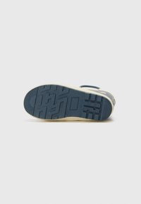 Semelle de sneaker en caoutchouc bleu avec un motif de grip texturé. Dispose d'un bord de couleur clair et d'un logo sur le côté, indiquant un design sportif.