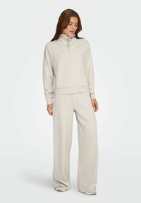 Lys grå sweatshirt med kvart lynlås og matchende bukser med brede ben i blødt stof. Har ribbede mansjetter og talje med en afslappet pasform.