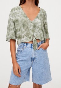 Chemise courte à manches courtes teinte en vert, avec un col en V et une fermeture à boutons, accompagnée d'un bermuda en denim bleu clair.